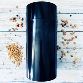 Large black seed storage vault container with vacuum-seal top on white wooden surface with scattered seeds